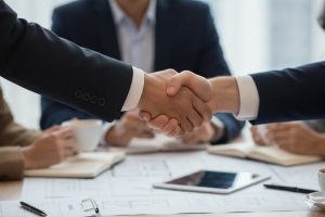 A close-up of two business professionals shaking hands over a signed contract and a pen on a glass desk, symbolizing a successful partnership or deal.